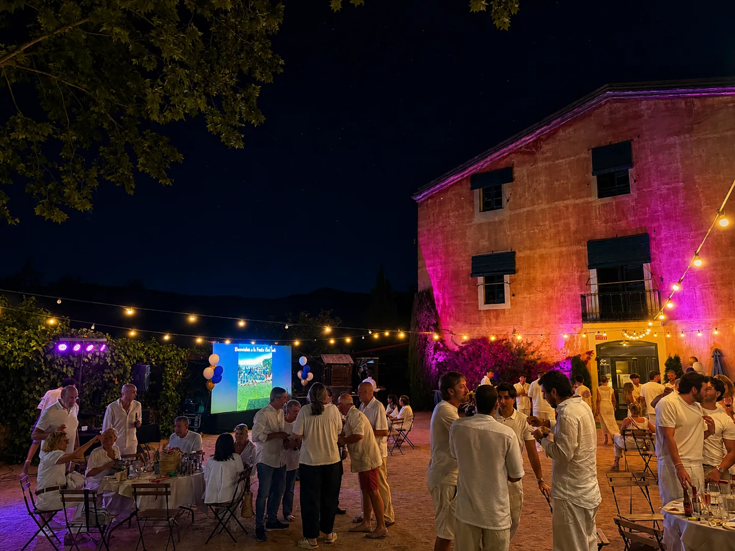 Pantalla LED encendida con contenido de bienvenida en el patio de la masía de Alella, con guirnaldas e invitados durante el evento corporativo