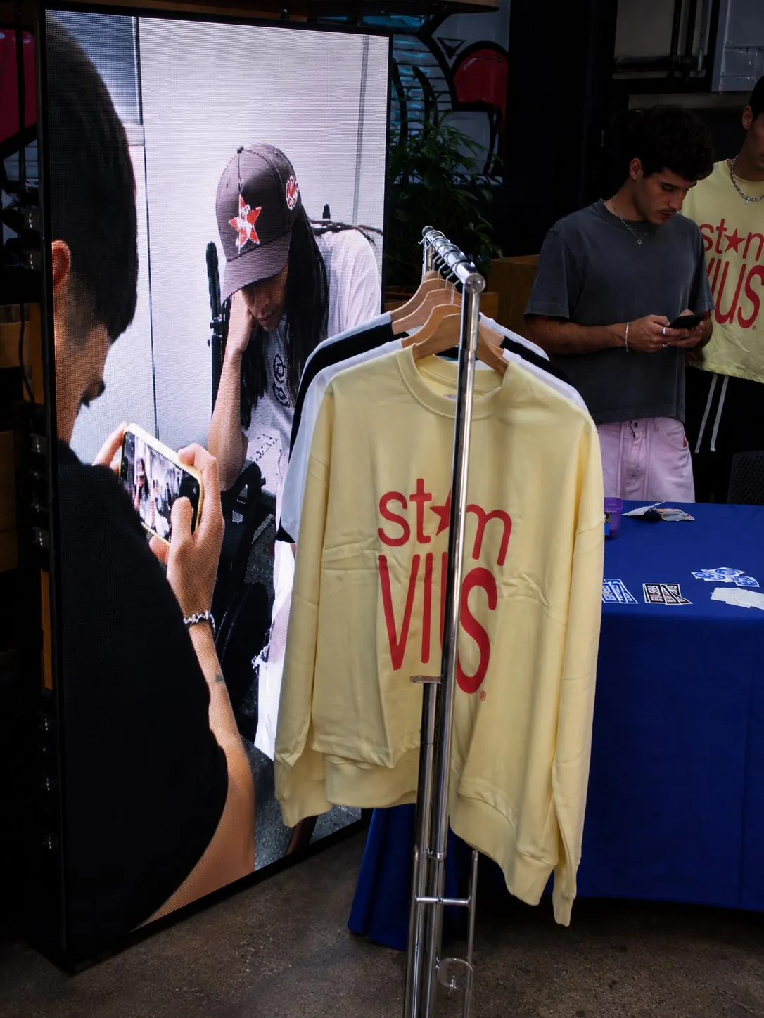 Tótem LED con contenido STEMVIUS junto a la sudadera amarilla de la marca en percha