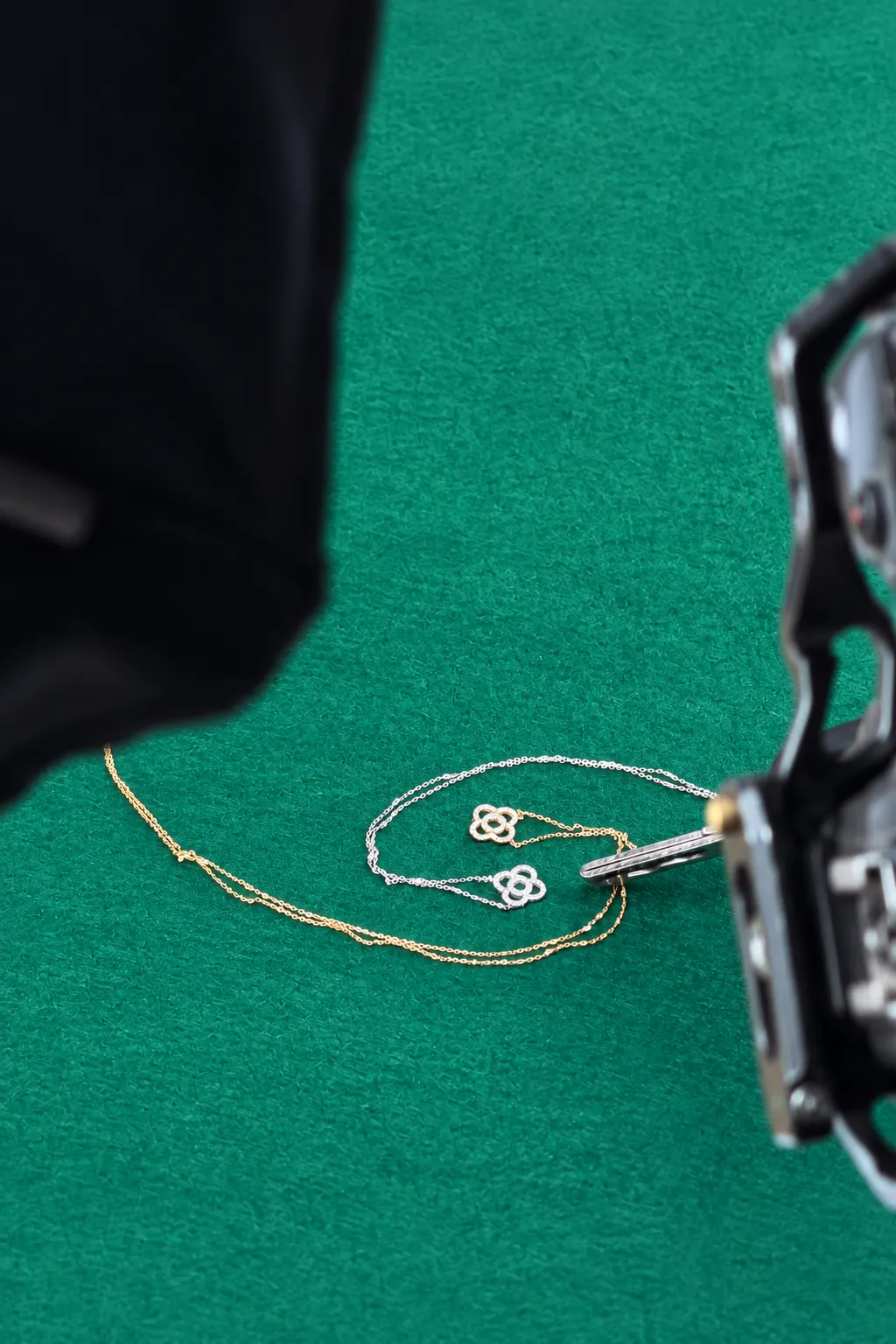 Objetivo macro a pocos centímetros de un collar con dos colgantes de flor sobre fieltro verde