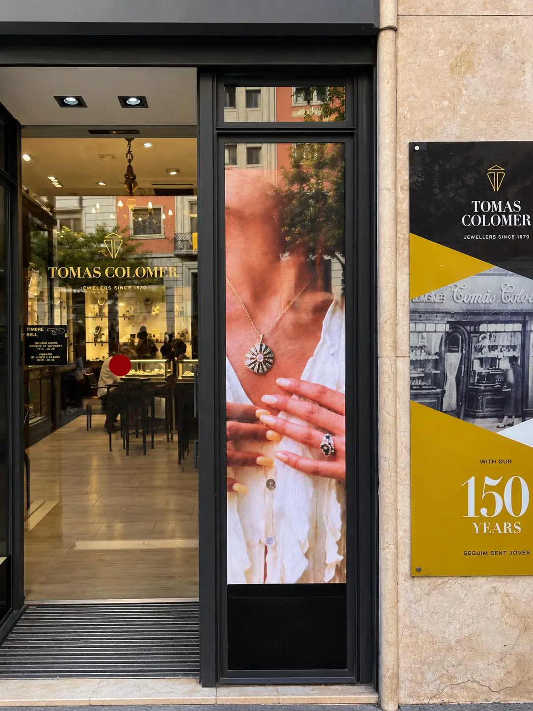 Pantalla LED vertical de Tomas Colomer encajada en la carpintería de la entrada, junto a la puerta y la placa del 150 aniversario