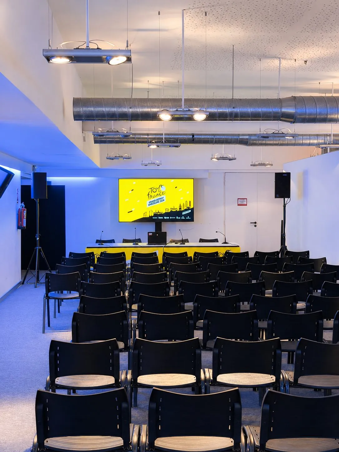 Segunda sala de prensa con iluminación ambiental azul, pantalla de refuerzo y sistema de conferencia